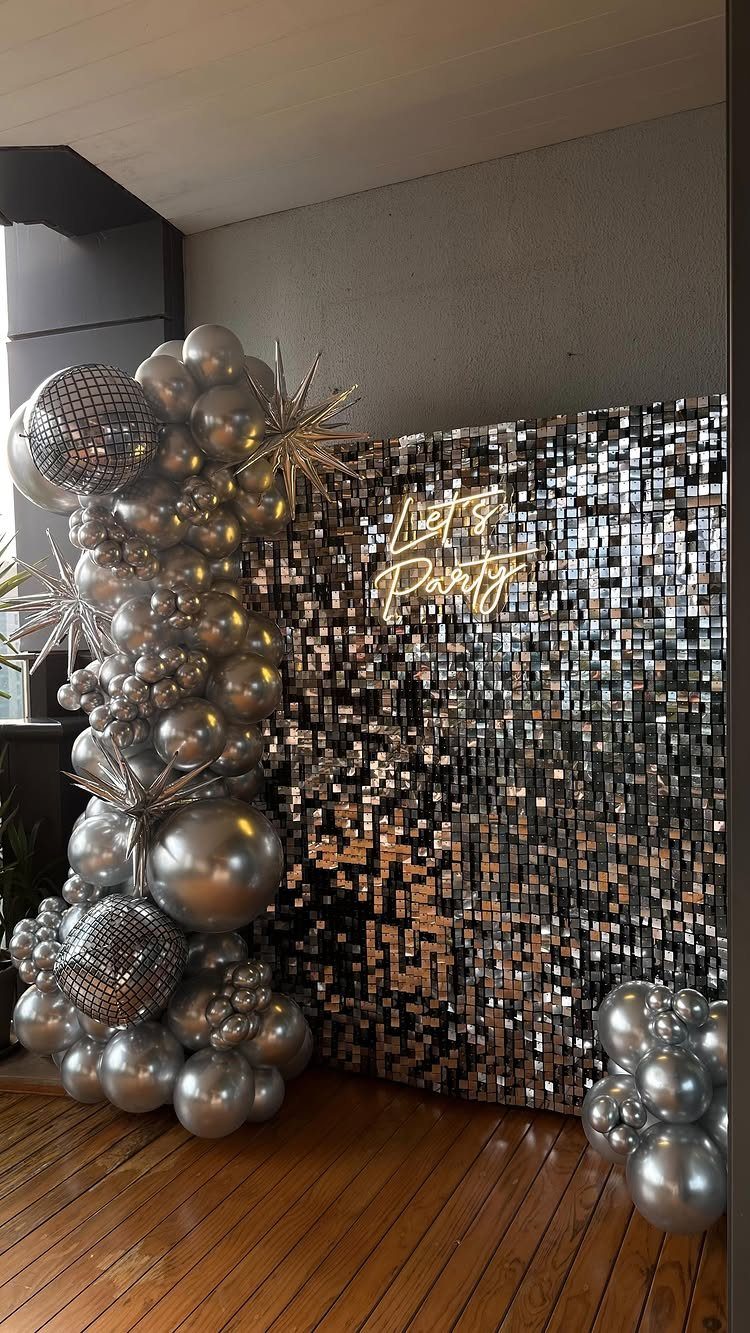 Silver sequin backdrop with neon sign and silver disco ball balloon garlands.