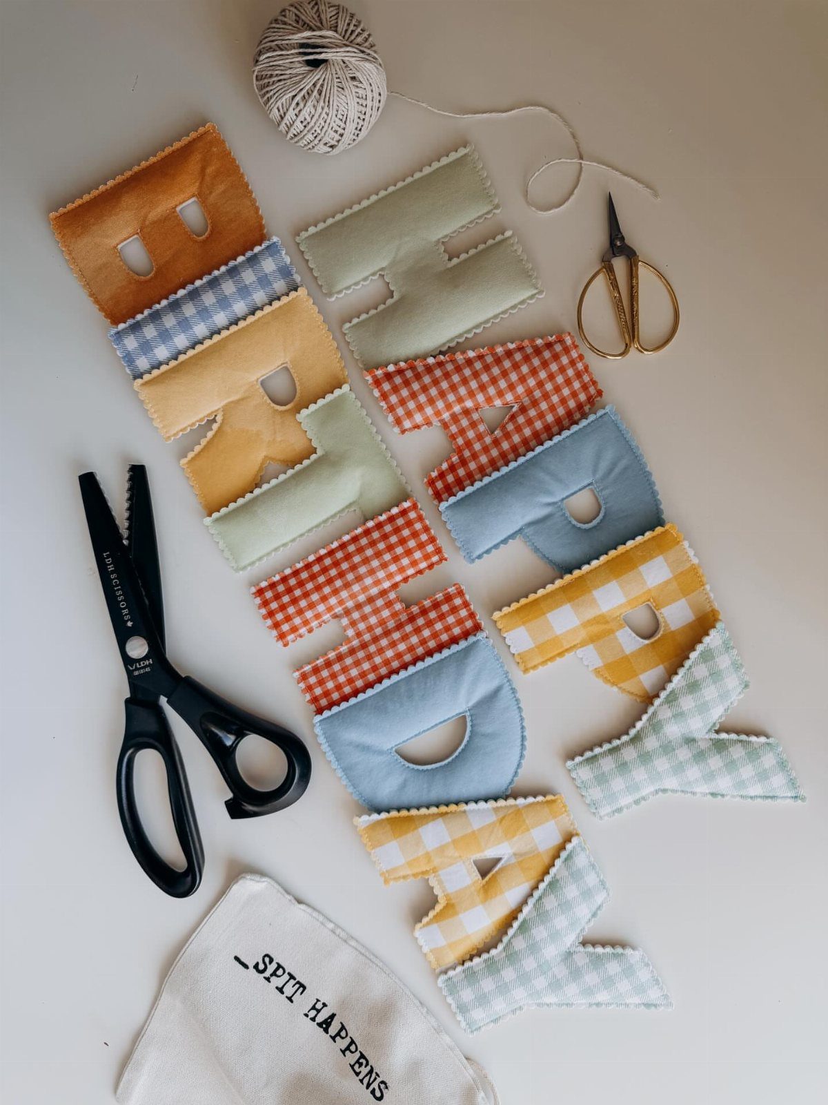 Fabric letters spelling Happy Birthday in mixed patterns with sewing tools on white.