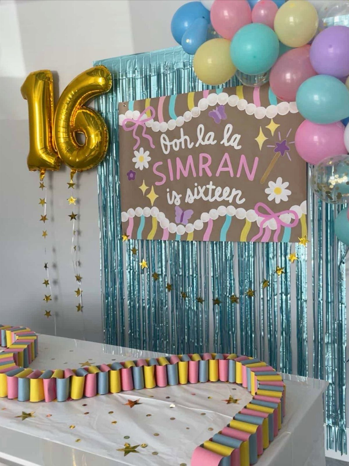 Birthday party decorations with gold 16 balloons, colorful balloons, and a custom sign.