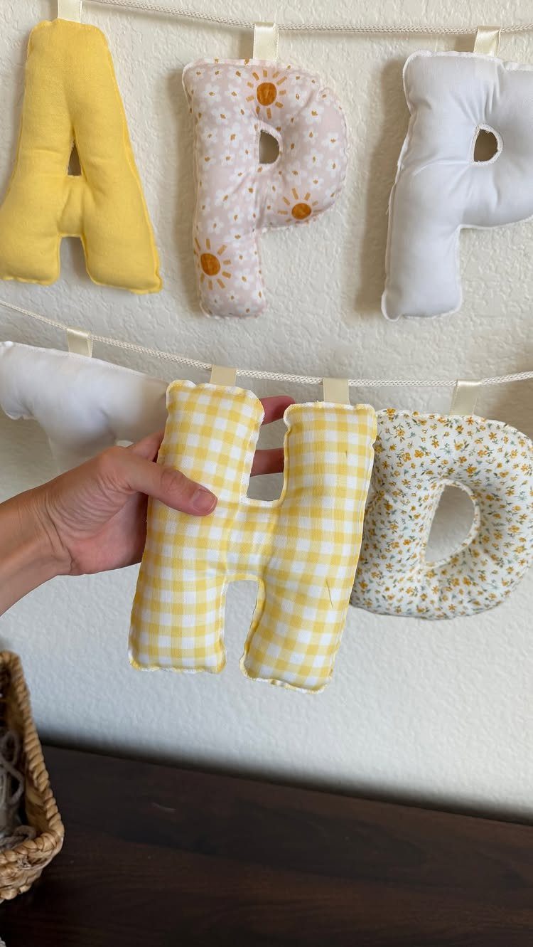 Stuffed fabric letters in yellow and floral patterns hanging on a string banner.