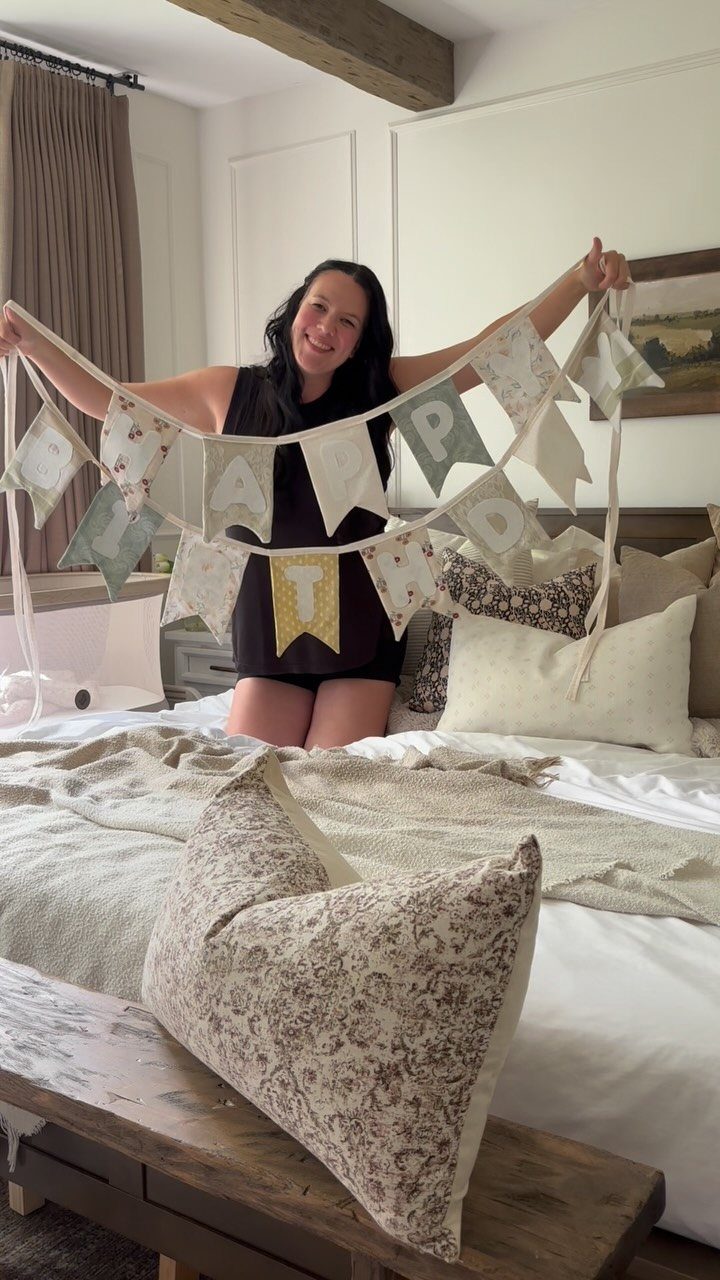 Woman holding a handmade fabric banner with floral triangular flags over a bed.