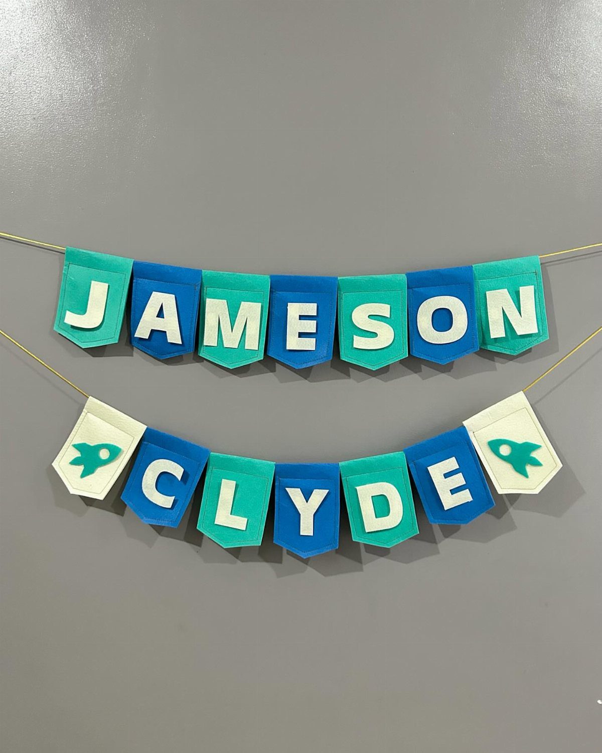 Fabric birthday banners spelling Jameson Clyde with white letters on blue and teal flags.