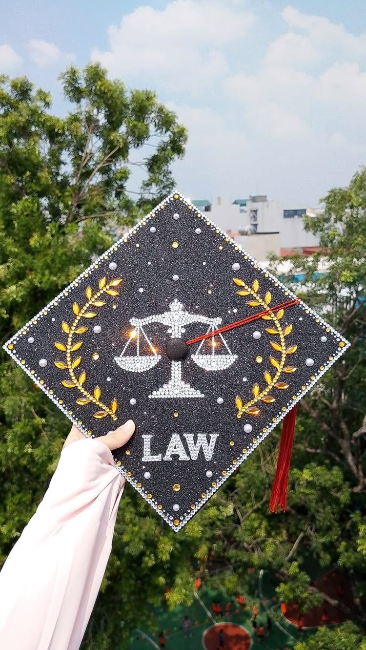 Decorated black graduation cap with law scales, gold leaves, and LAW text.