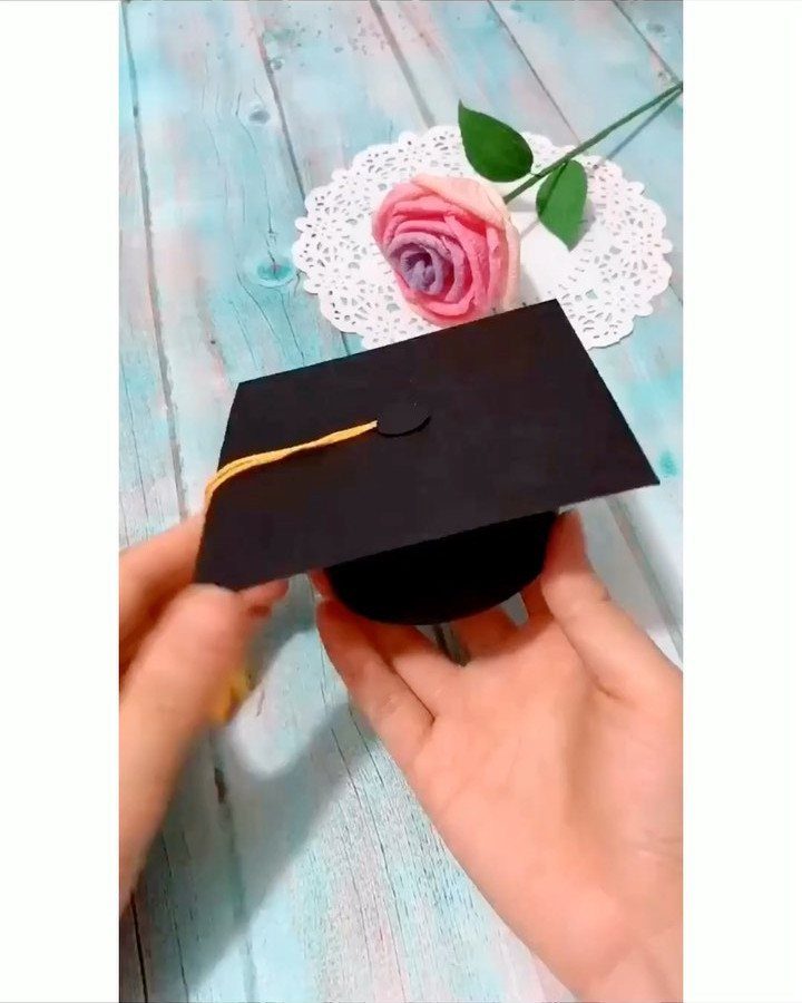 Handmade black graduation cap with yellow tassel held over a blue wooden background