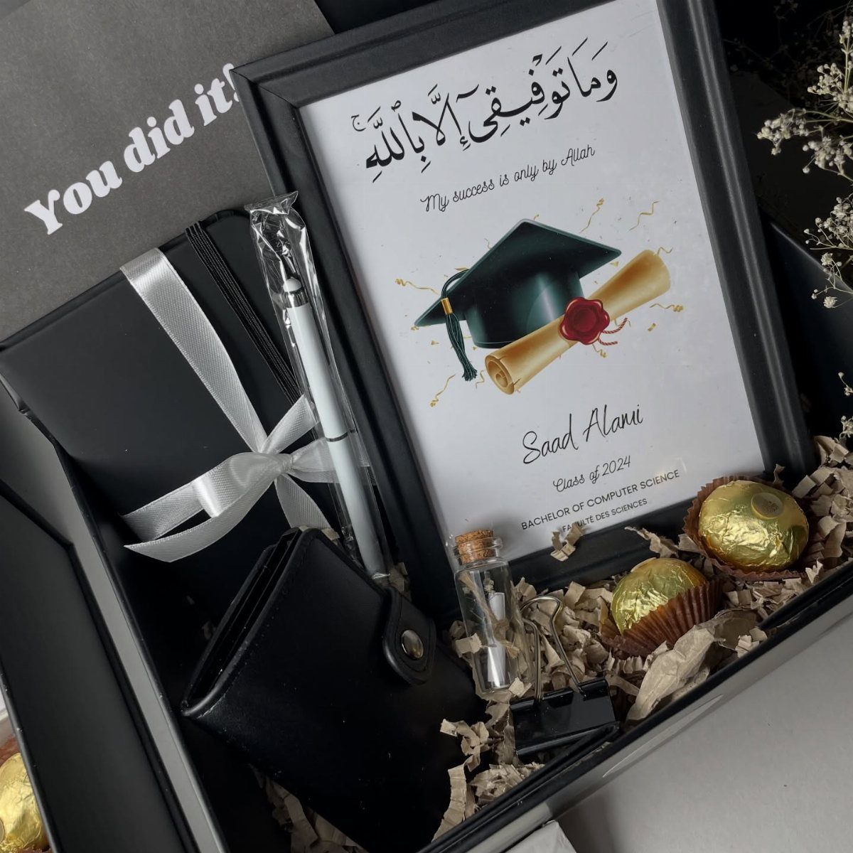 Graduation gift box with framed certificate, white pen, wallet, and gold chocolates.