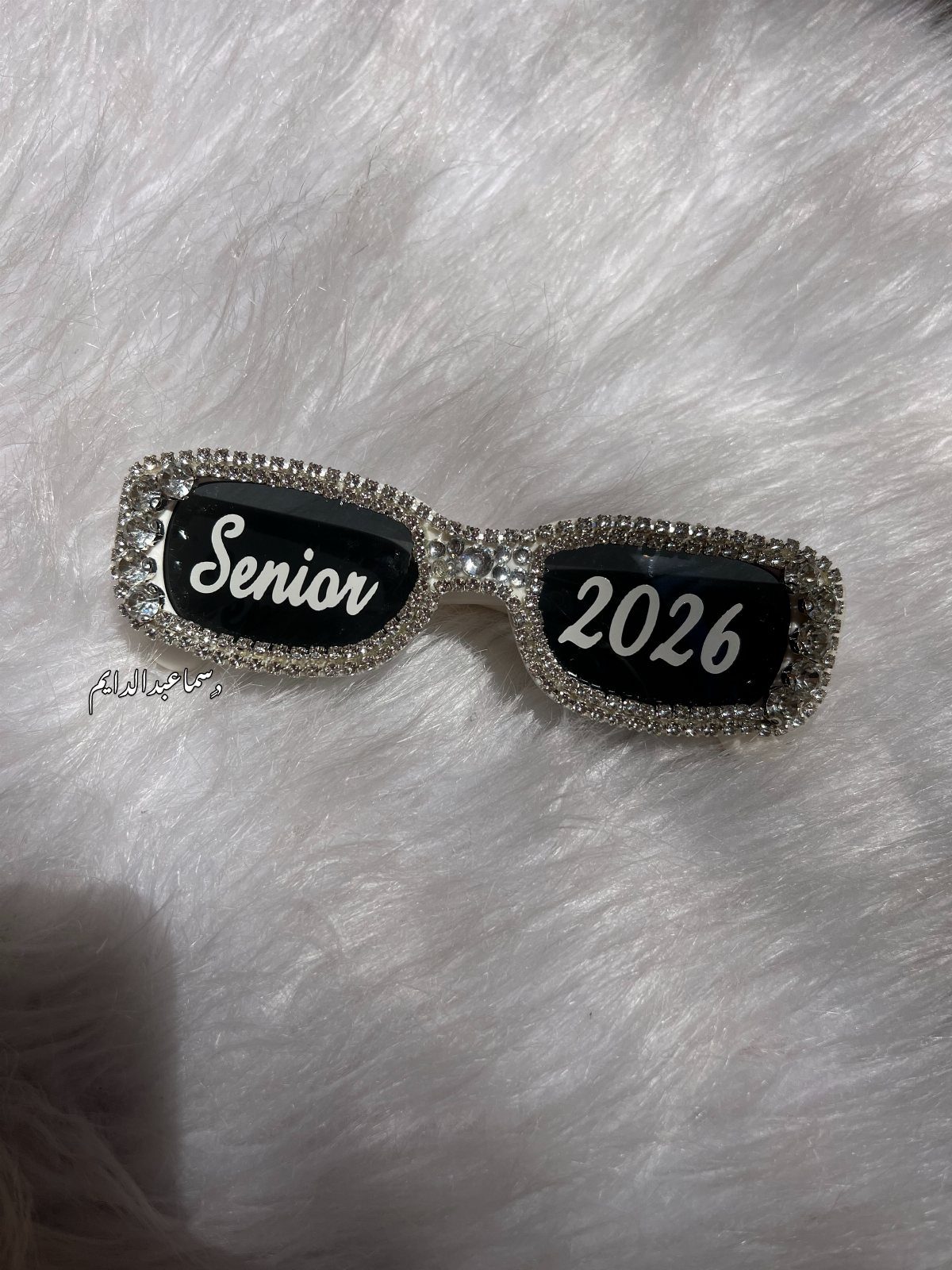 Rhinestone sunglasses with Senior 2026 written on the lenses on white fur.