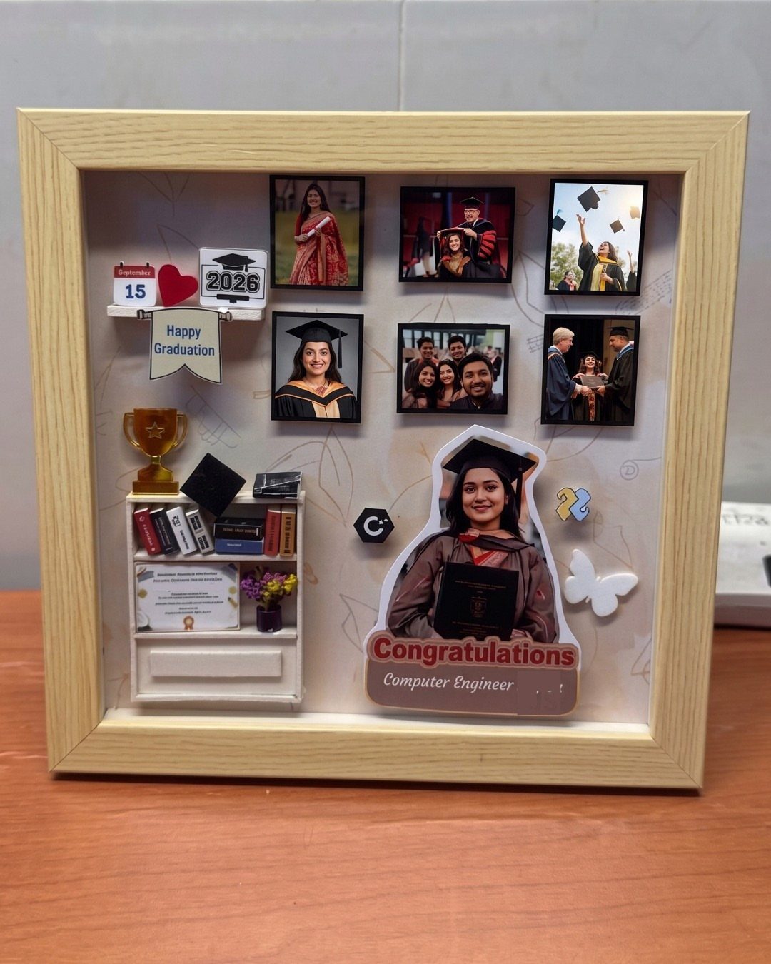 Graduation shadow box frame with photos, miniature bookshelf, and congratulations message.