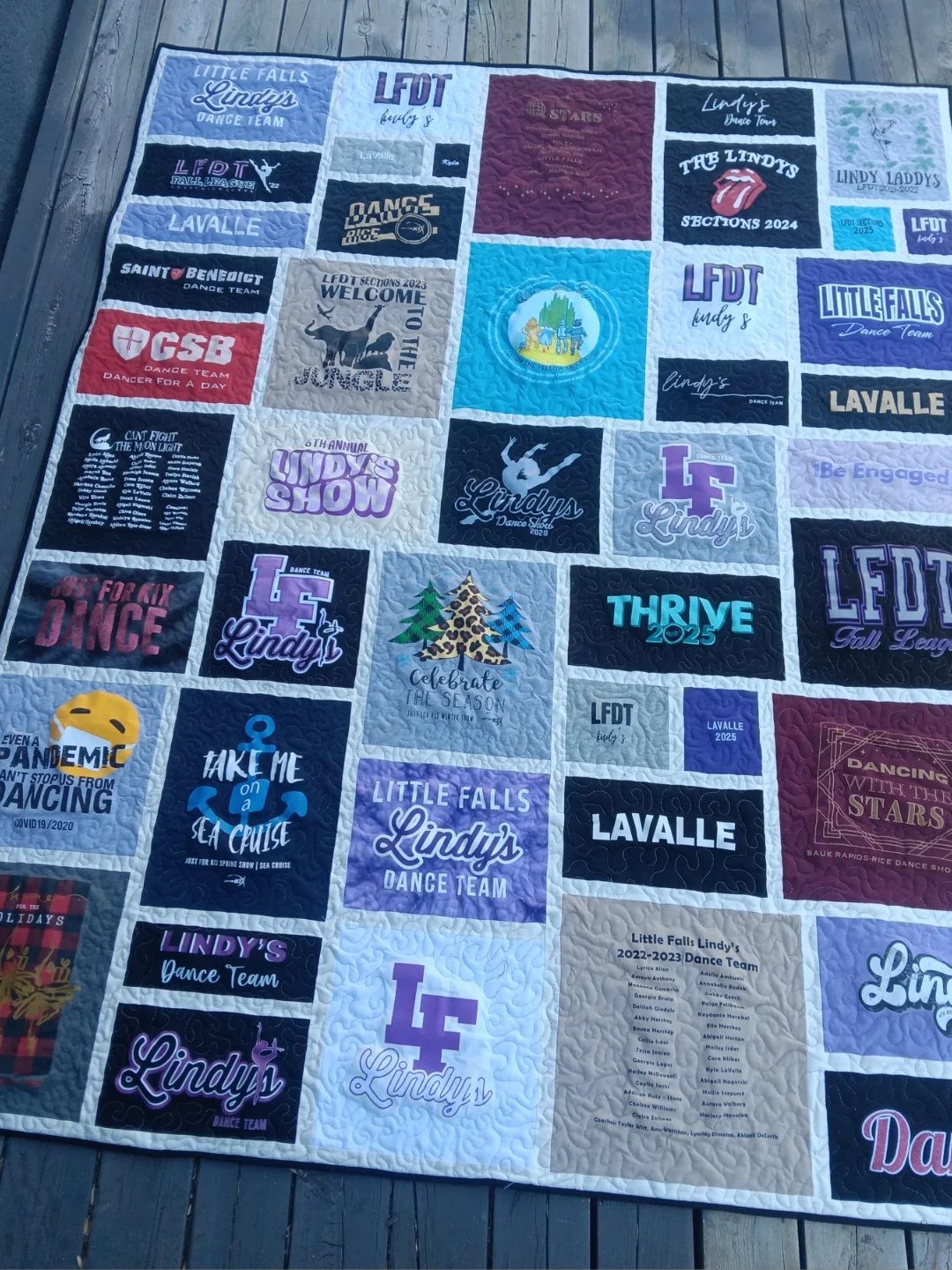 T-shirt quilt made from colorful dance team shirts laid on a wooden deck.