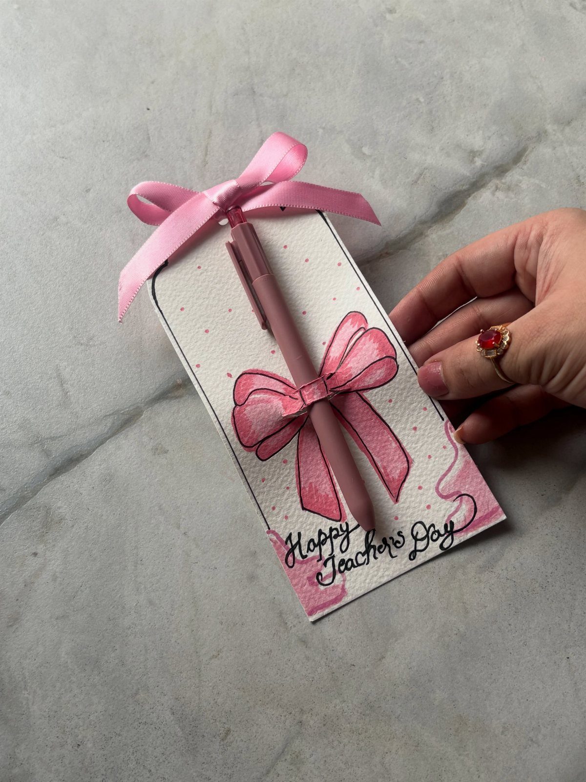 Pink pen attached to a Happy Teacher's Day card with a pink bow.