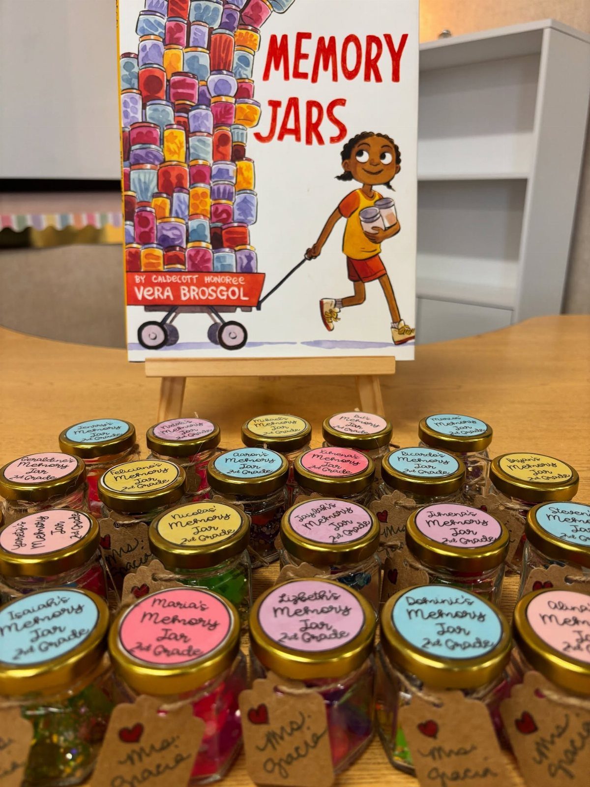 Small glass memory jars with colorful lids and labels arranged before a book.