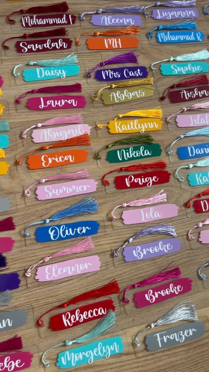 Colorful personalized bookmarks with tassels and names arranged on a wooden table.