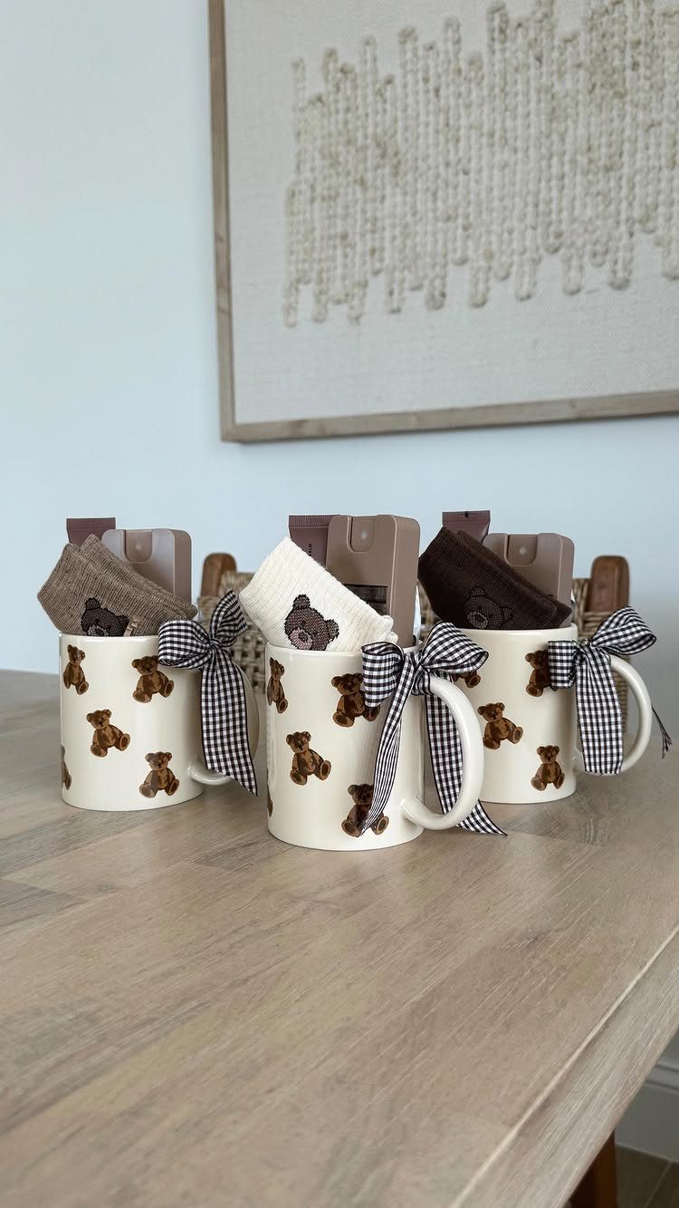 Three teddy bear patterned mugs with checkered bows containing small gift pouches.