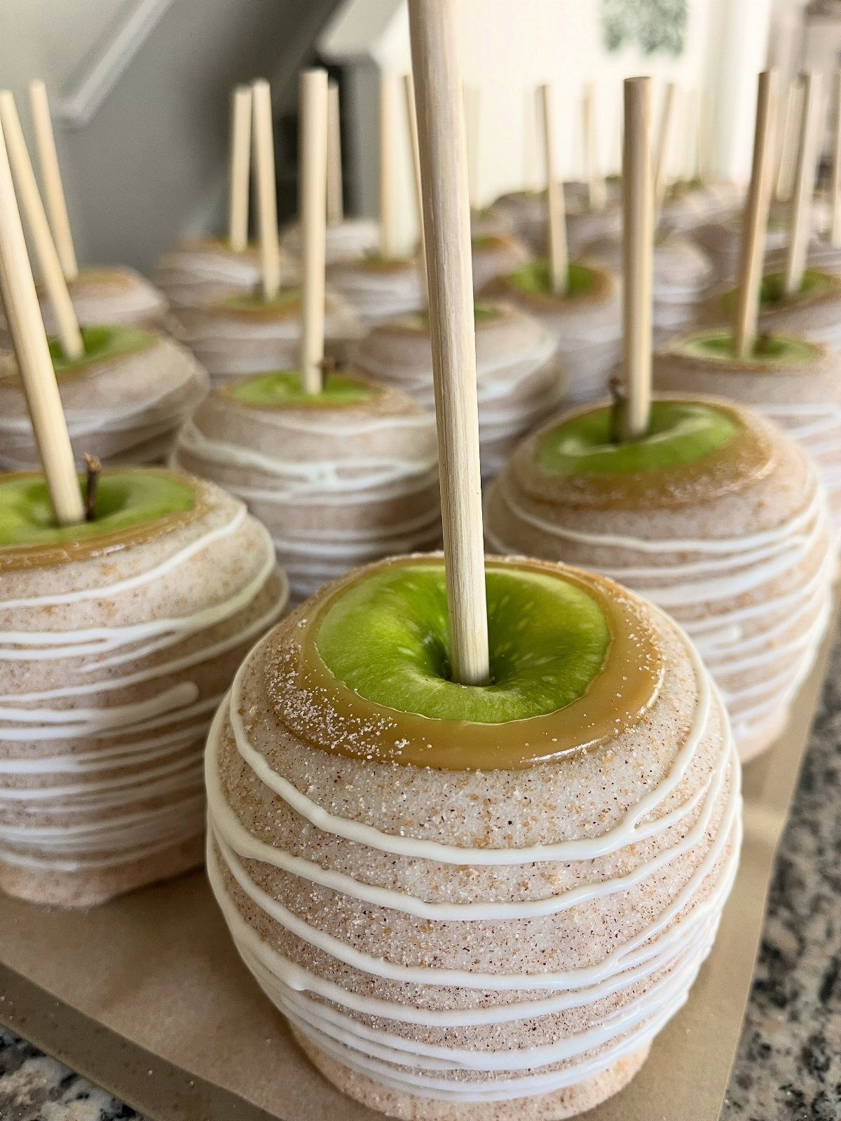 Caramel apples coated in cinnamon sugar and white icing on a tray