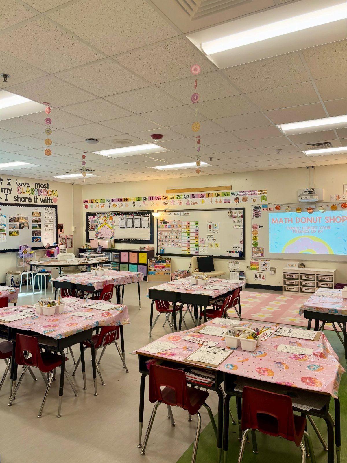 Elementary classroom decorated with pink donut patterns on tables and hanging ceiling garlands.