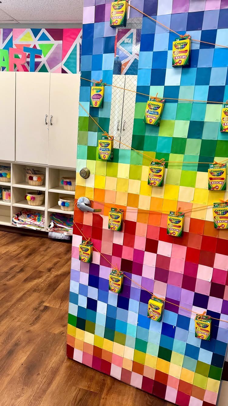 Rainbow colored square tiles on a classroom wall with snacks clipped to strings.