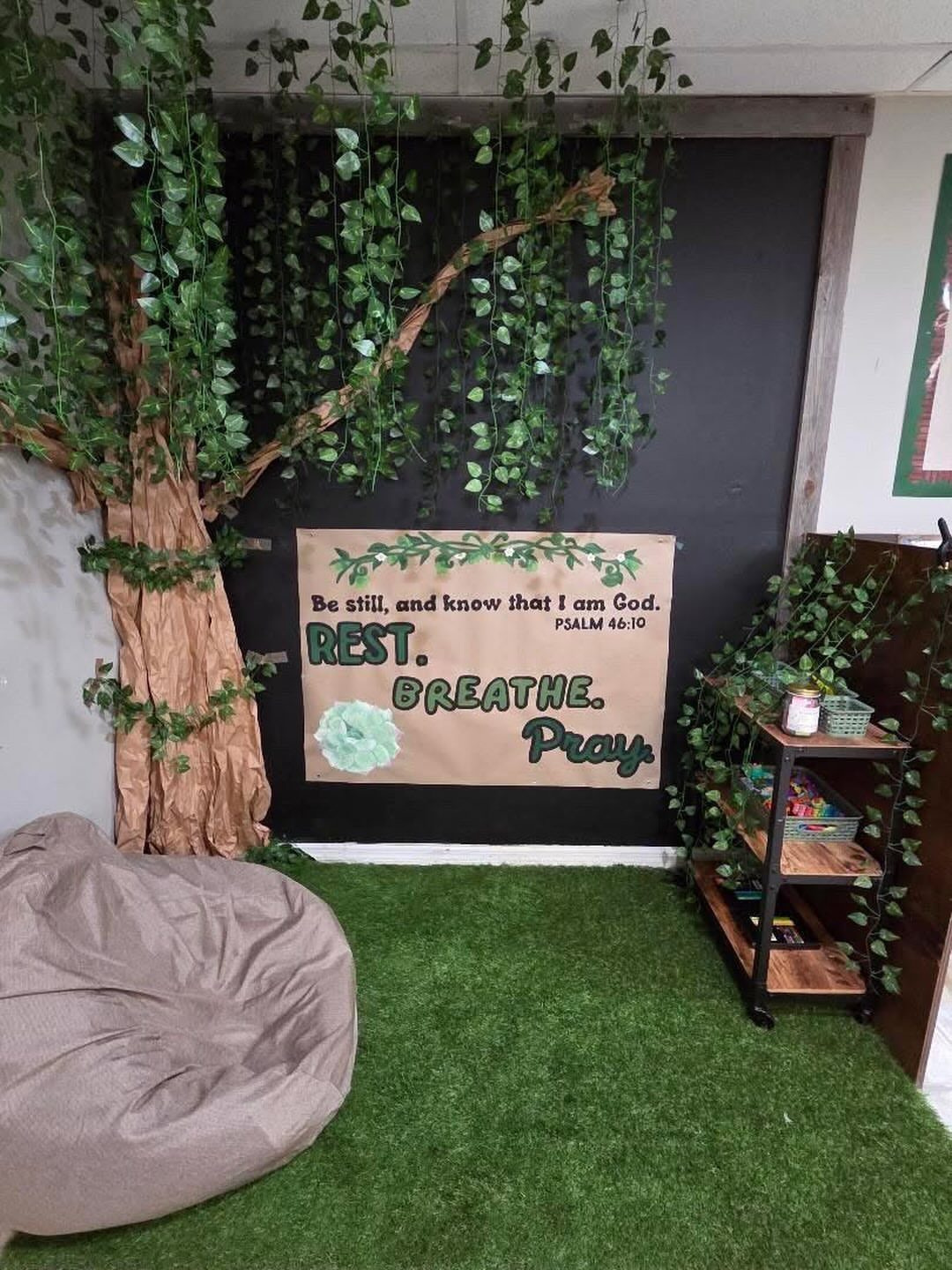 Faux tree and artificial grass in a classroom reading nook with a banner.