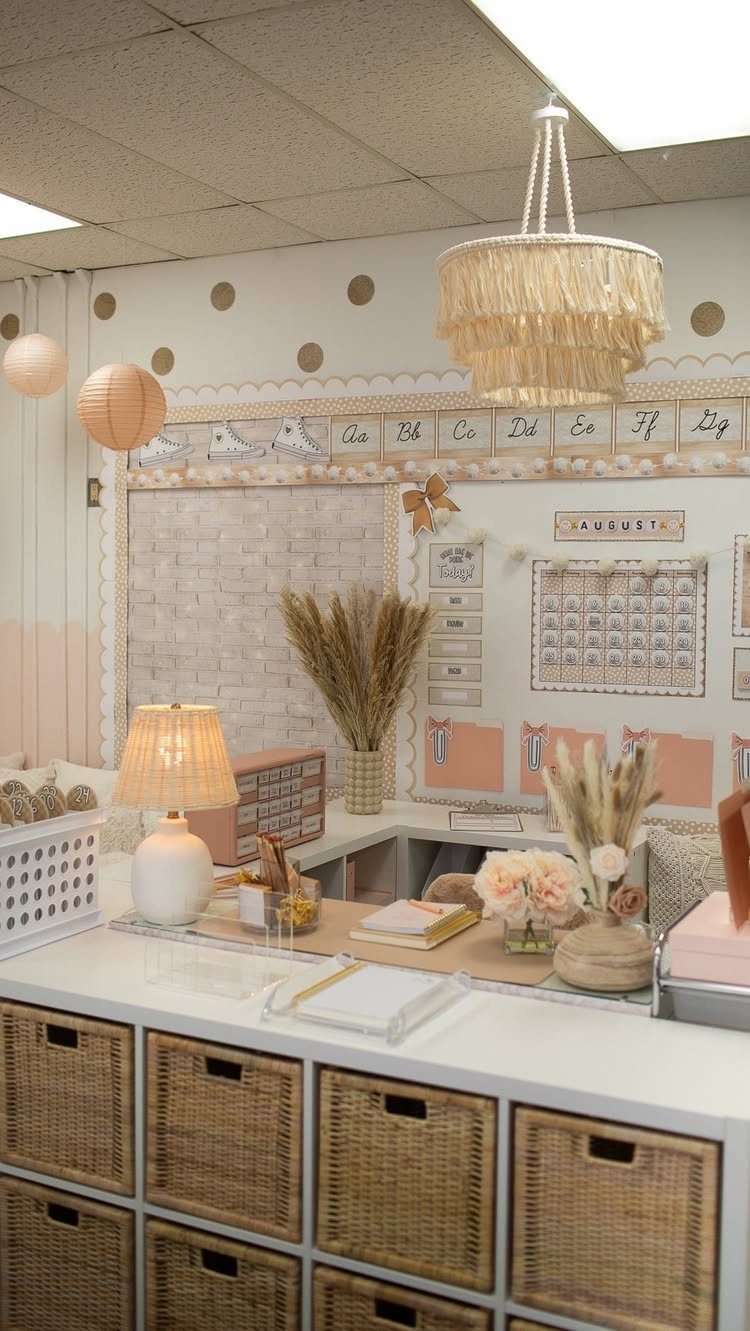 Neutral classroom workspace with wicker bins, dried grass, and a fringed chandelier.