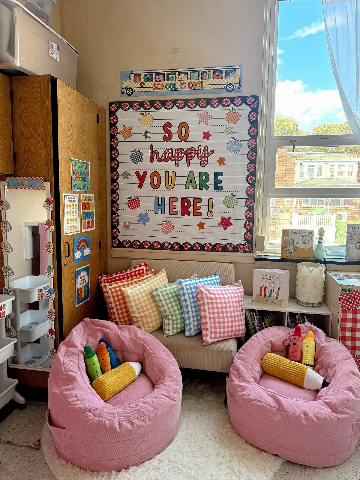 Classroom reading nook with pink beanbags and colorful plaid accent pillows on a sofa.