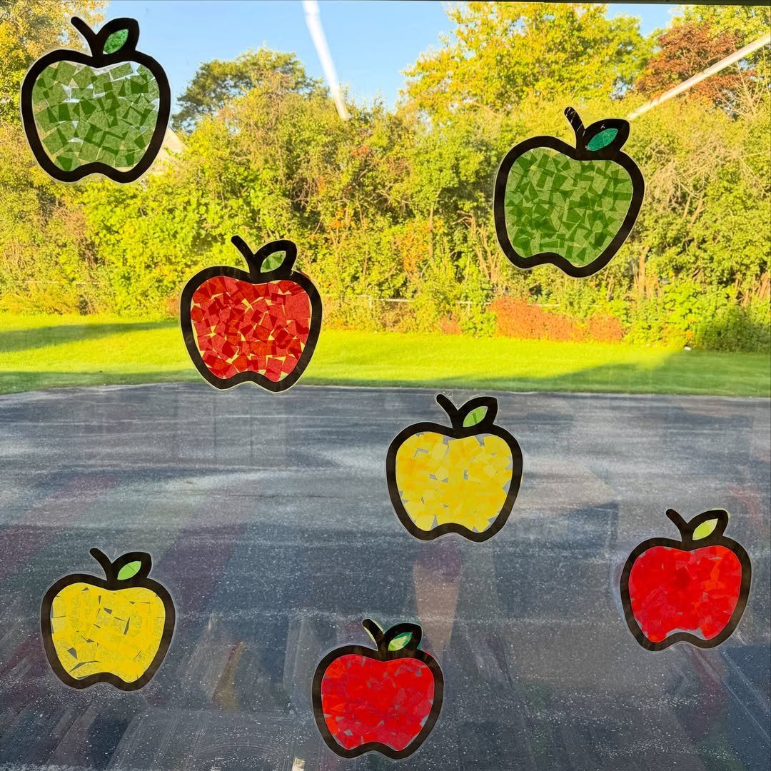 Colorful tissue paper apple crafts attached to a window overlooking autumn trees.