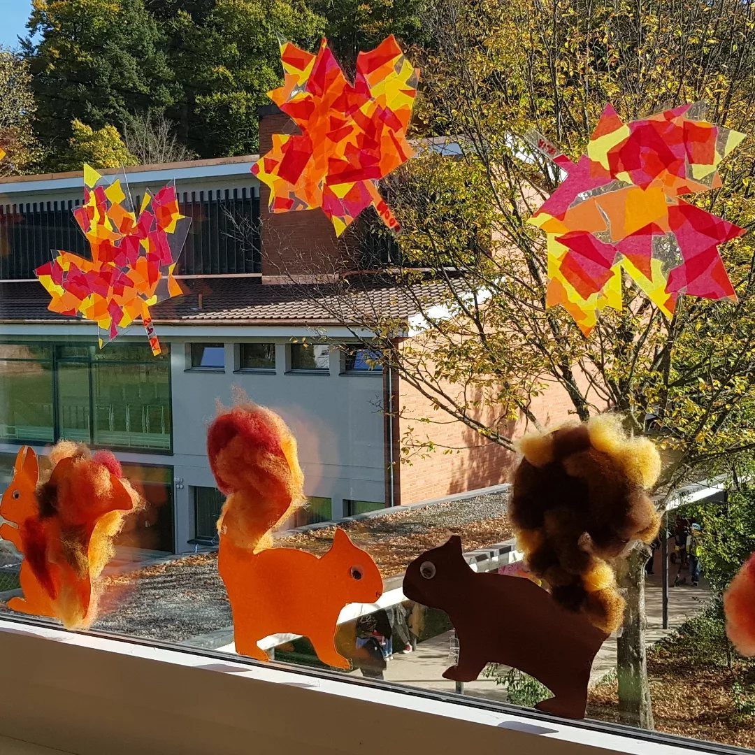 Autumn leaves and squirrels made of tissue paper and cardstock on a window.