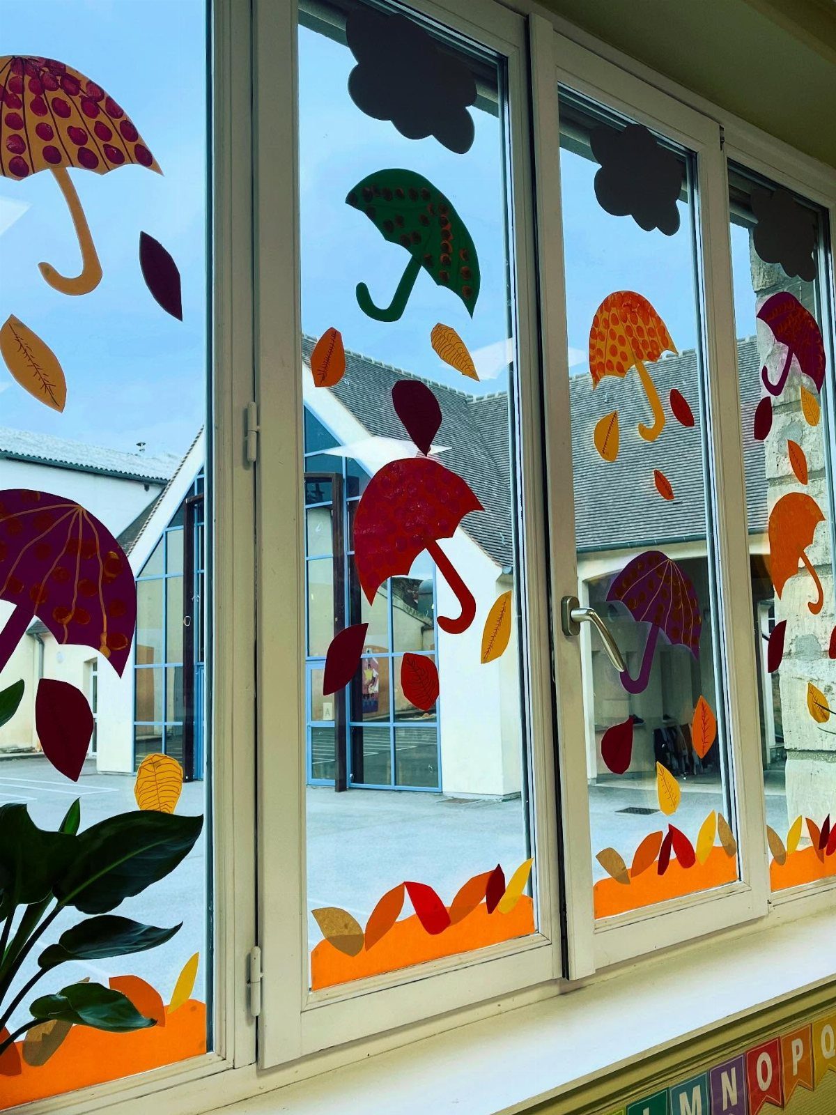 Colorful paper umbrellas and autumn leaves decorating white-framed classroom windows.