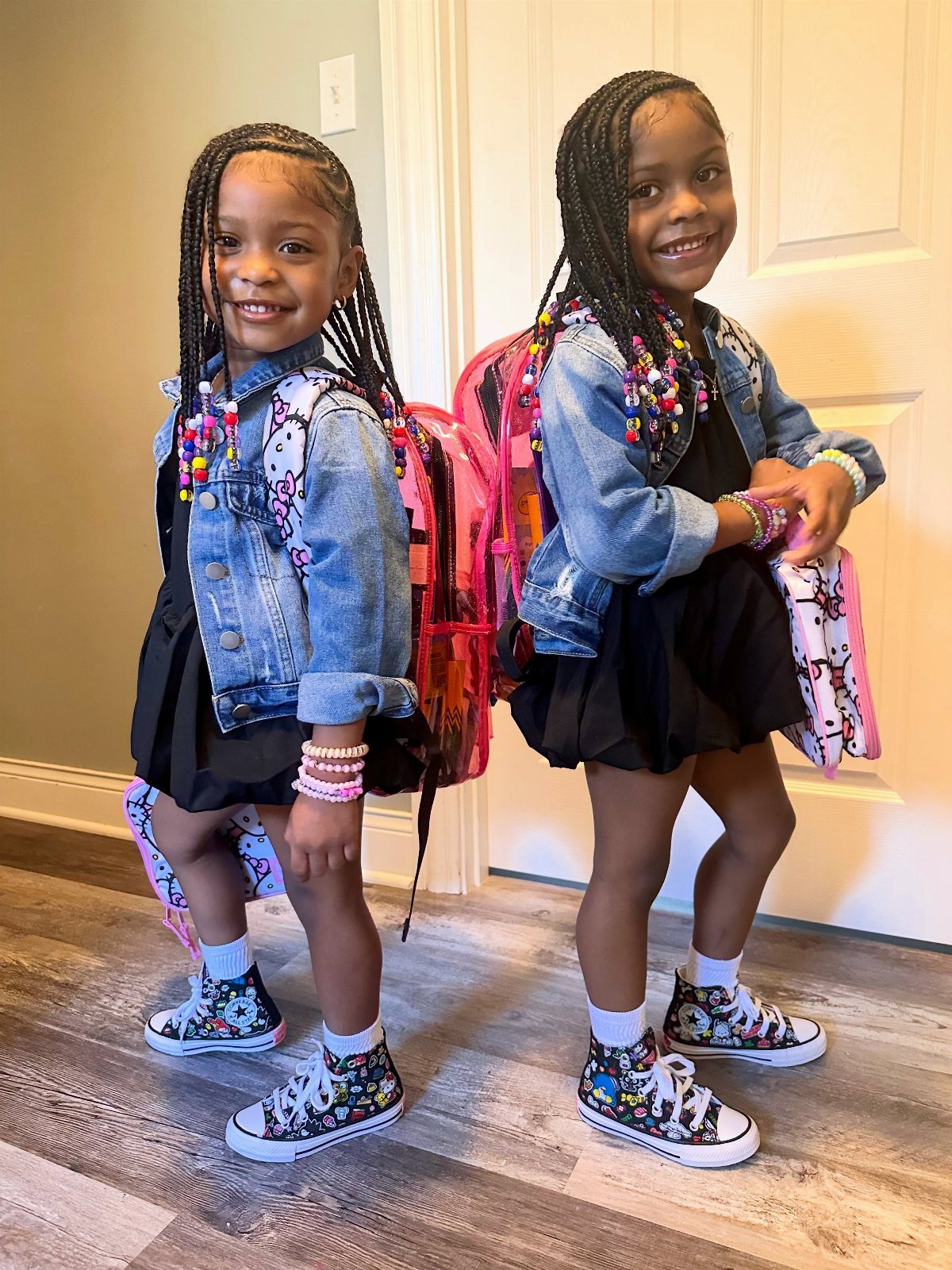 Two young girls wearing matching denim jackets and black dresses with pink backpacks.
