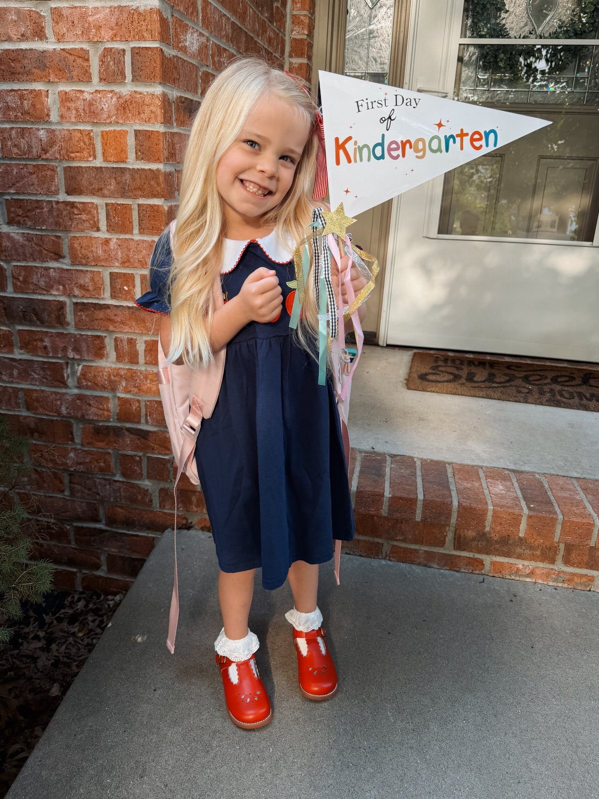 Young girl in navy dress and red shoes holding a kindergarten pennant flag.
