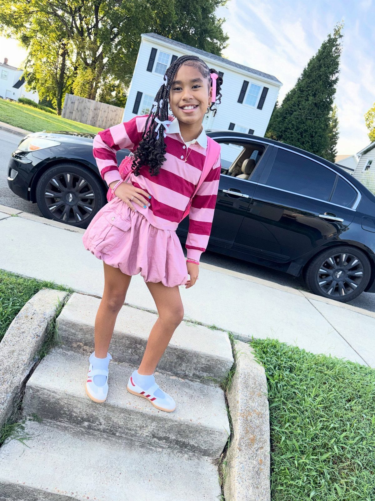 Young girl wearing a striped polo and pink skirt posing on outdoor steps