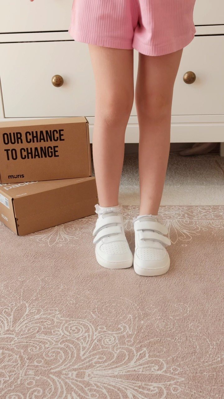 Child's feet wearing white velcro sneakers and pink shorts on a patterned rug.