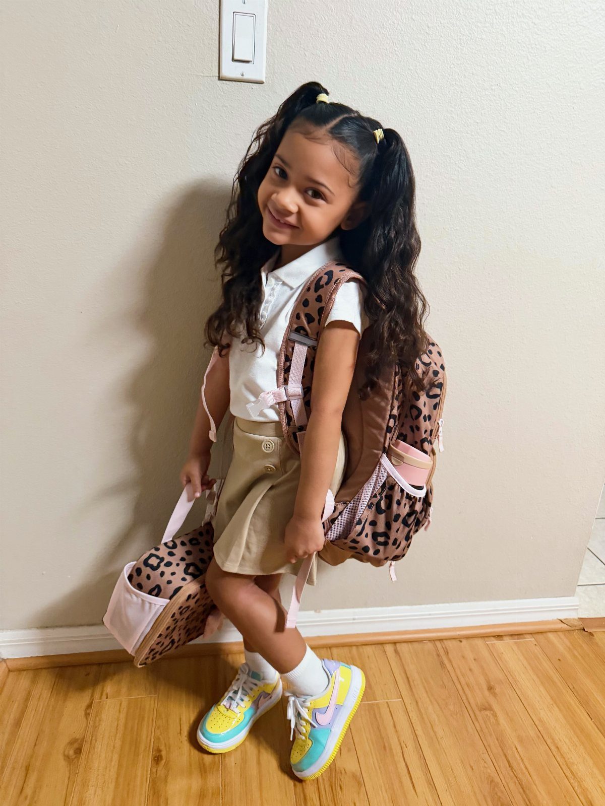 Young girl in a white polo and tan skirt with leopard-print backpack.