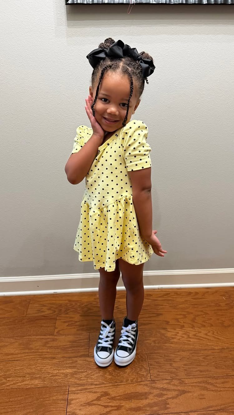 Young girl wearing a yellow polka dot dress and black high-top sneakers.