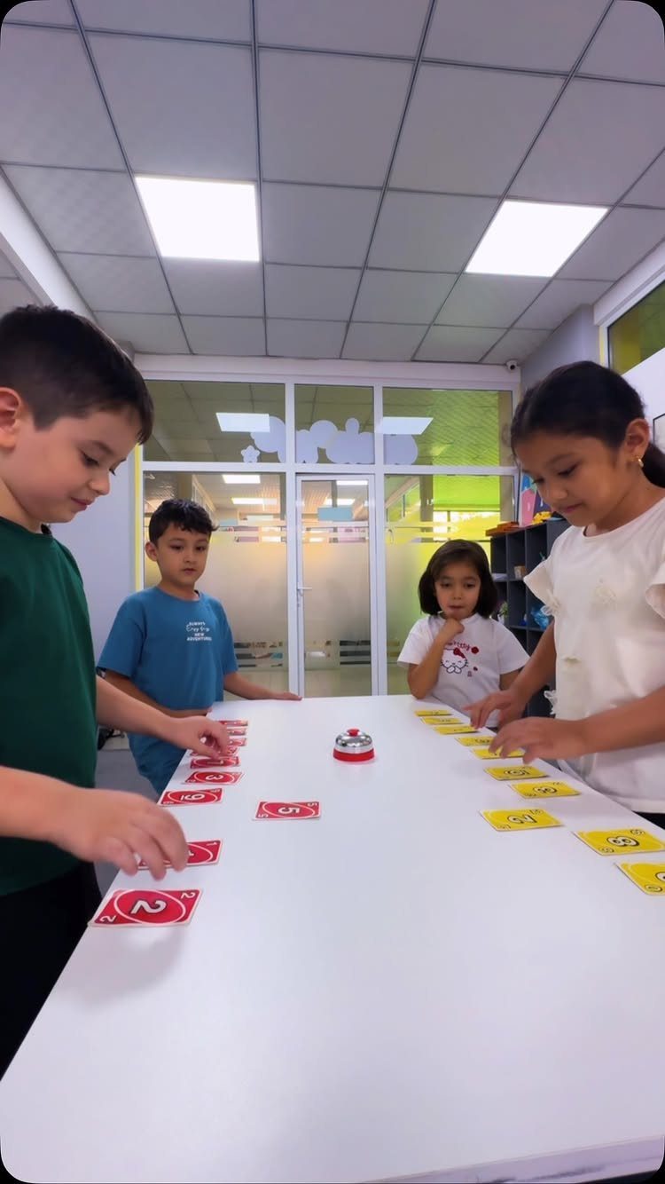 Children playing a card game with a buzzer on a white table.