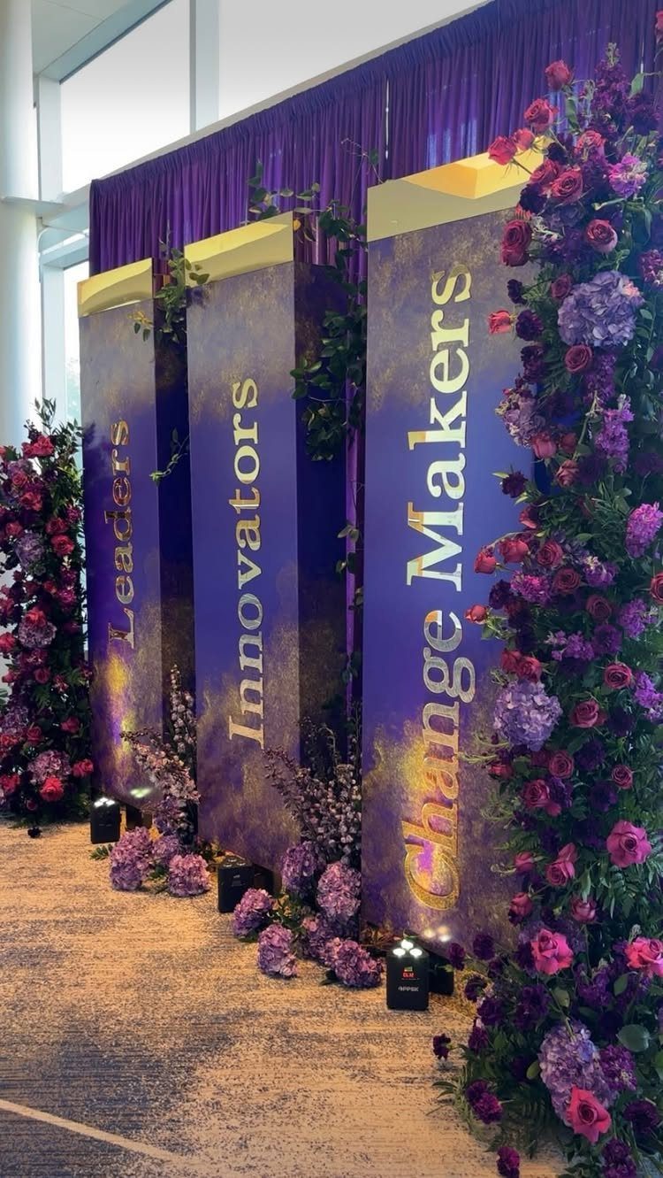 Purple event banners with gold text surrounded by purple and pink floral arrangements.
