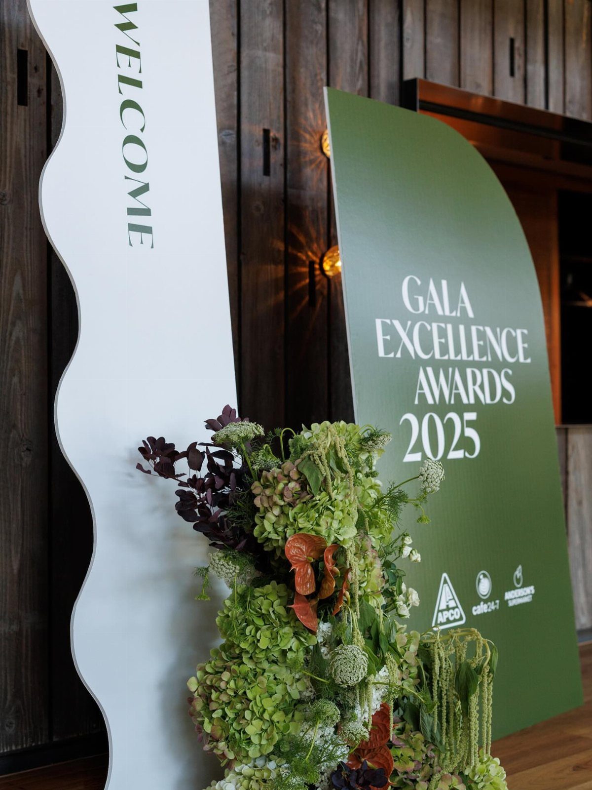 Gala awards entrance with green and white signage and lush floral arrangements.