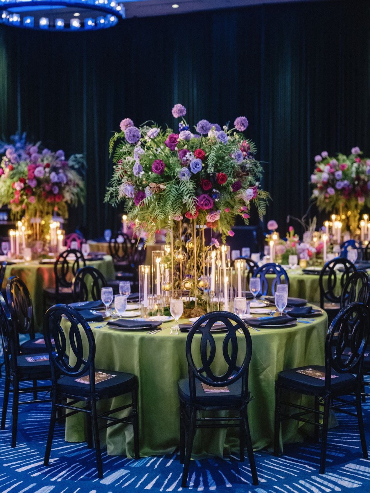 Tall floral centerpiece with purple and pink flowers on a green banquet table.