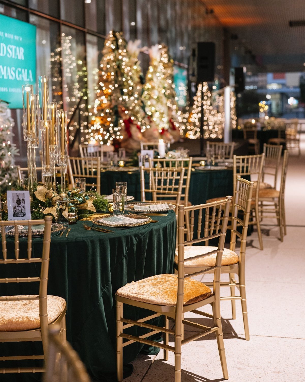 Green banquet tables with gold chairs and lit Christmas trees in the background.