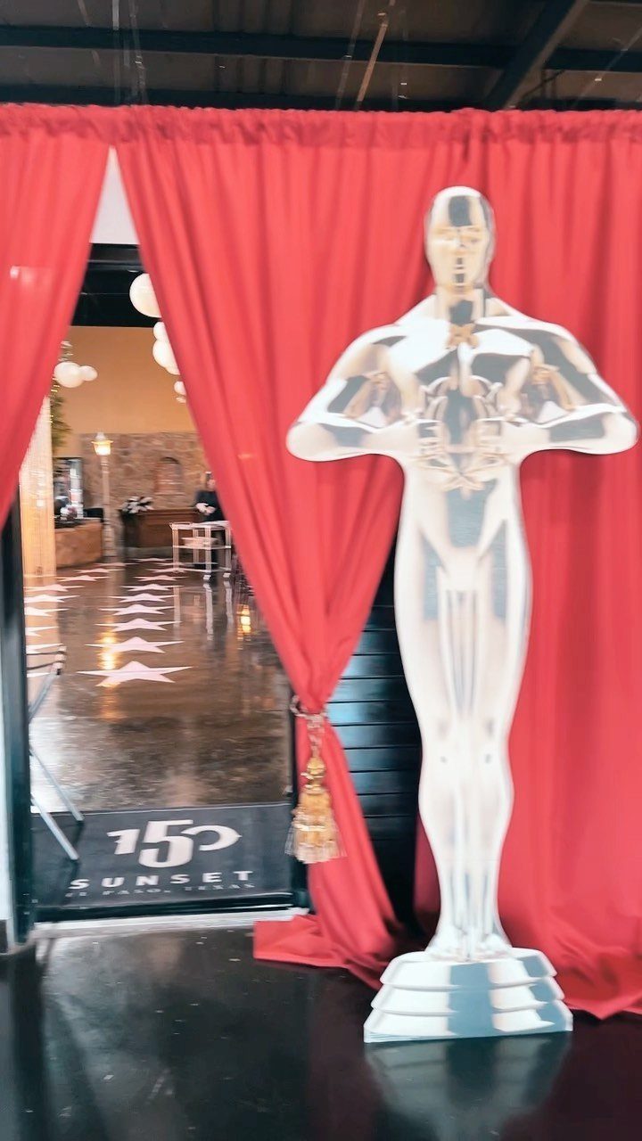Silver Oscar trophy statue standing before red curtains with star-patterned flooring.