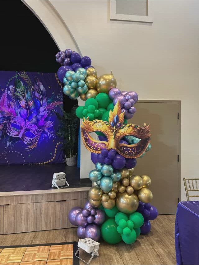 Purple, green, and gold balloon column with a large masquerade mask centerpiece.