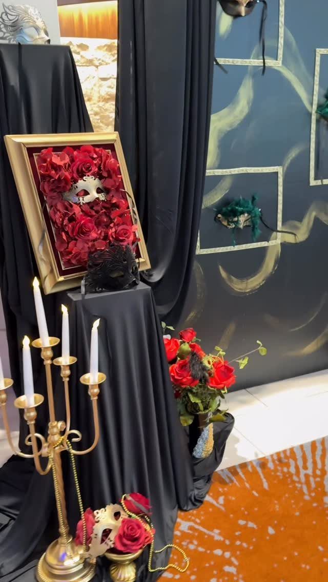 Masquerade masks and red roses displayed with a gold candelabra and black drapery.