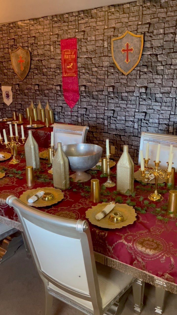 Medieval banquet table with red gold linens, gold plates, and shields on stone wall
