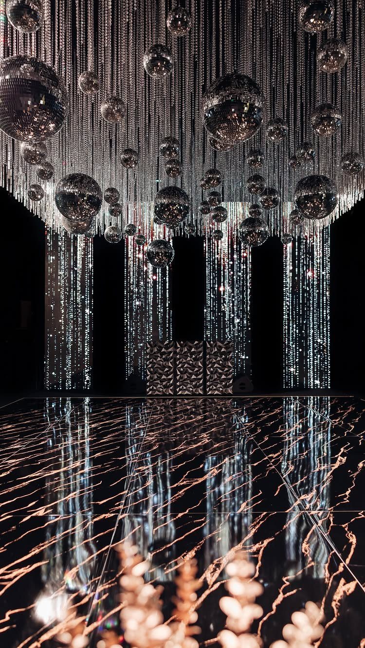 Mirrored disco balls and silver beaded curtains hanging over a reflective black floor.