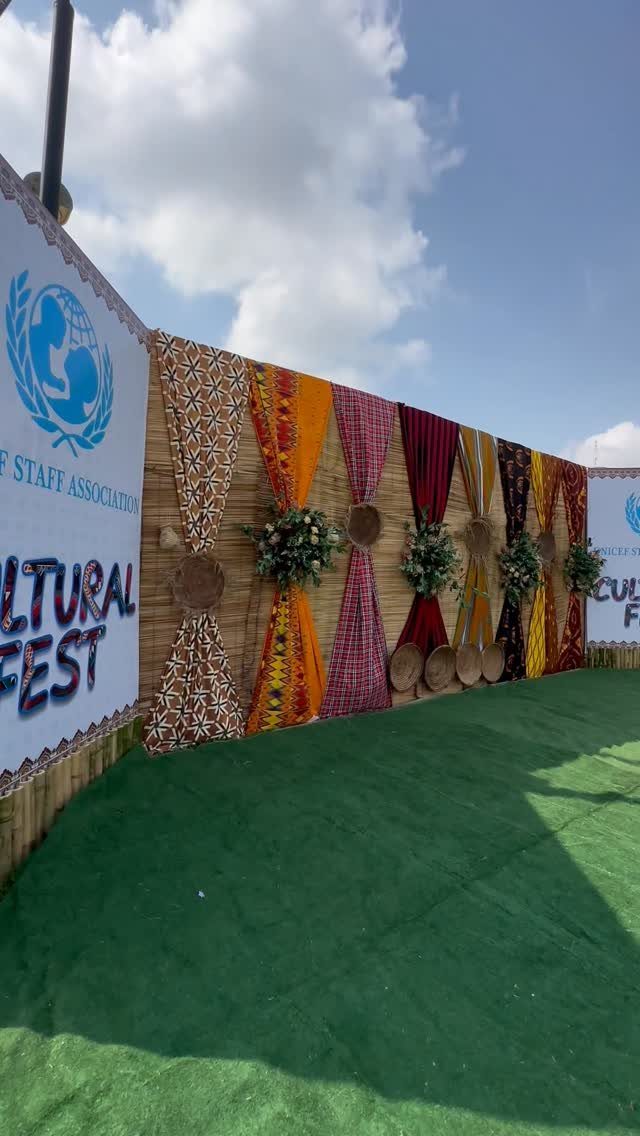 Colorful patterned fabric drapes with floral arrangements as an outdoor event backdrop.