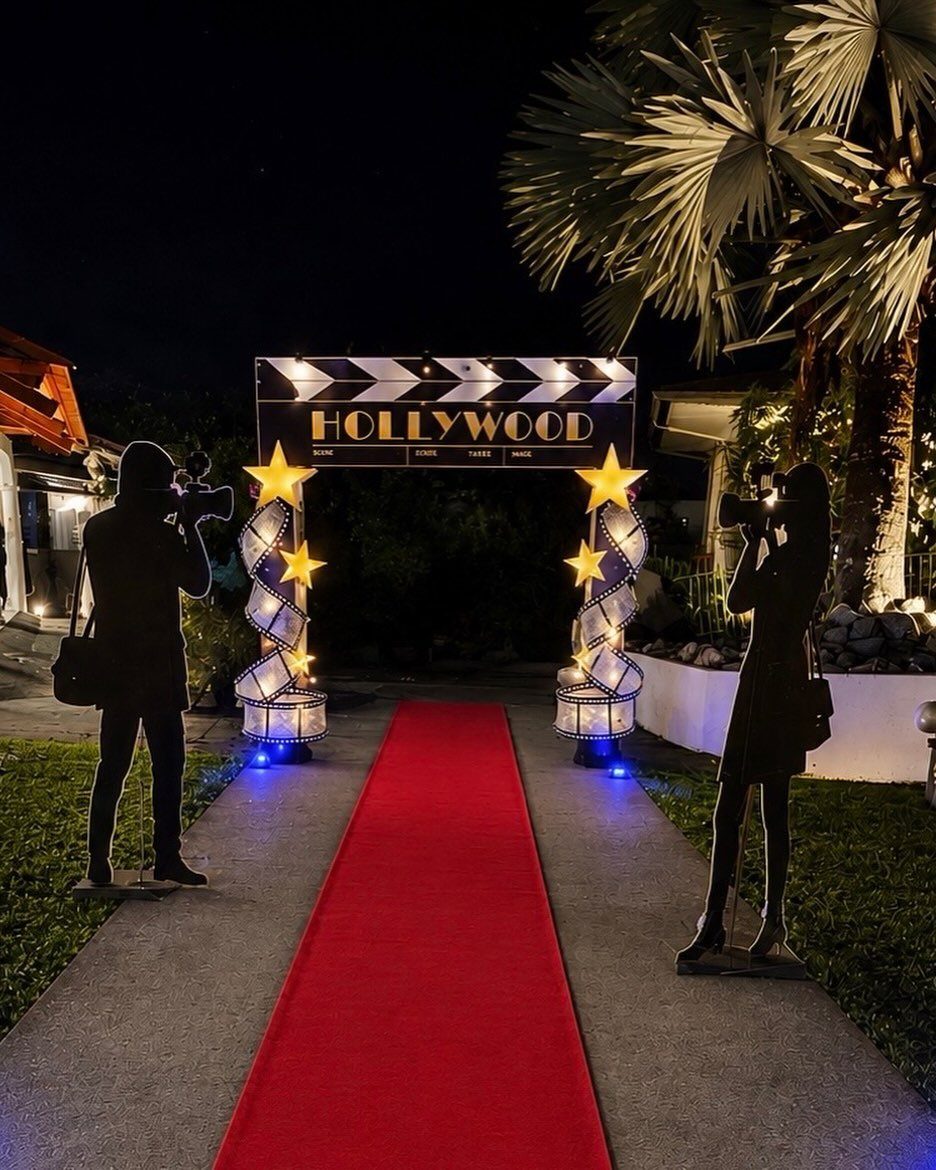 Red carpet entrance with Hollywood clapperboard sign and photographer silhouettes at night.