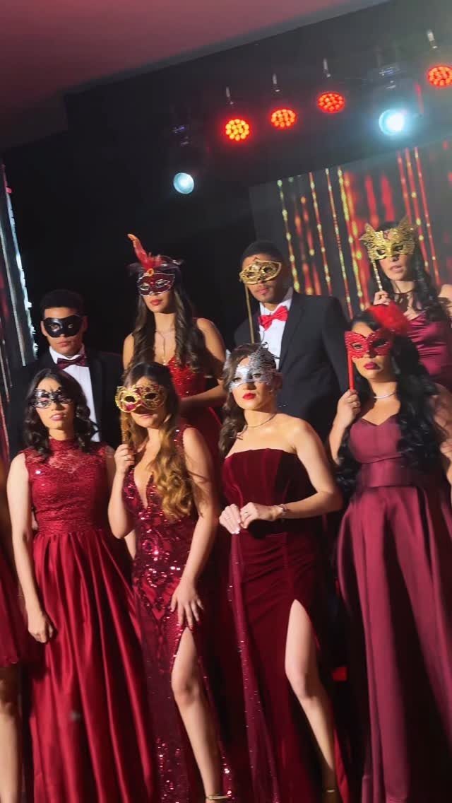Group of young adults in red gowns and tuxedos wearing masquerade masks.