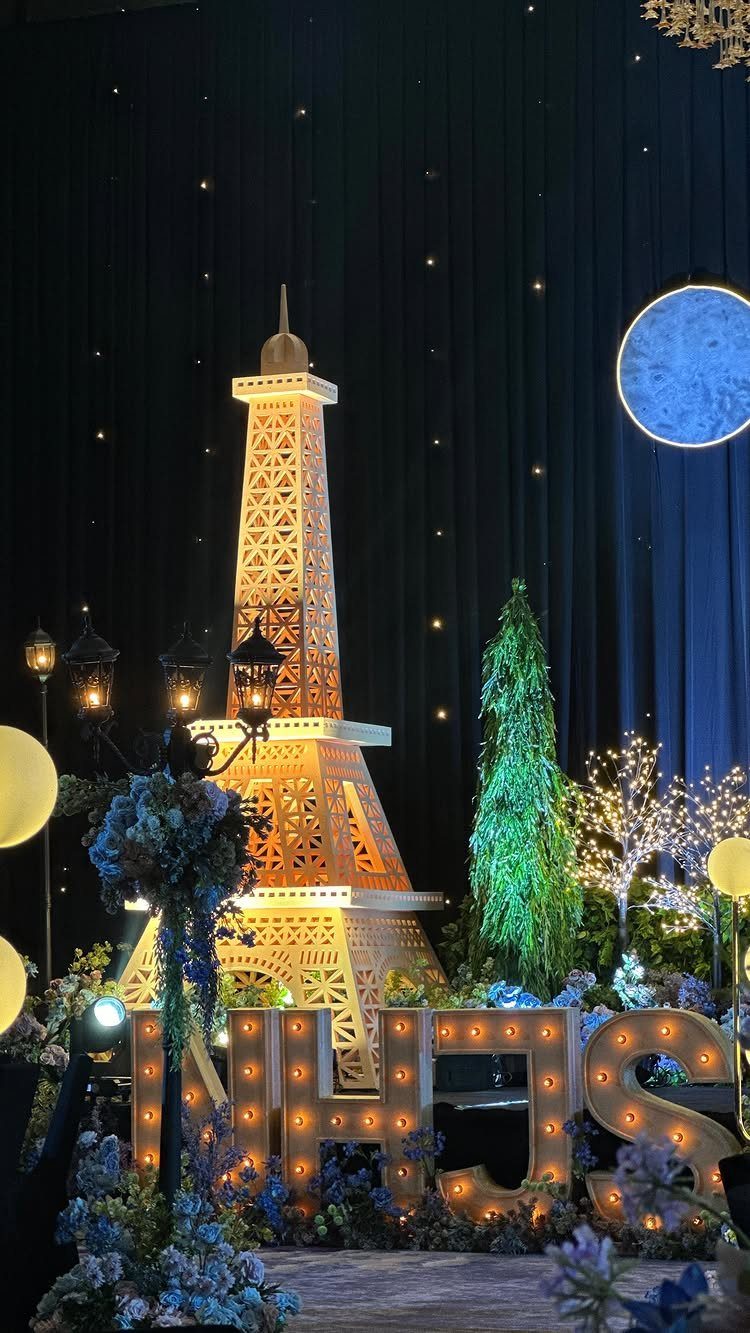 Illuminated Eiffel Tower model with NHS letters and blue floral decorations for an event.