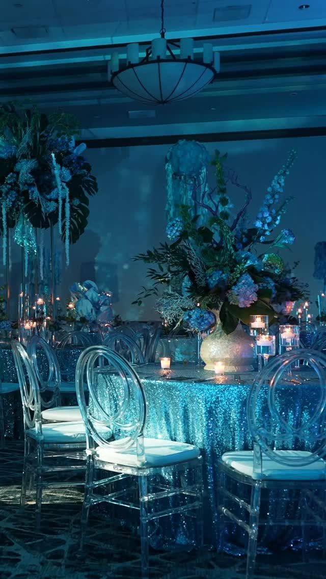 Blue sequined table with clear chairs and floral centerpieces in a themed ballroom