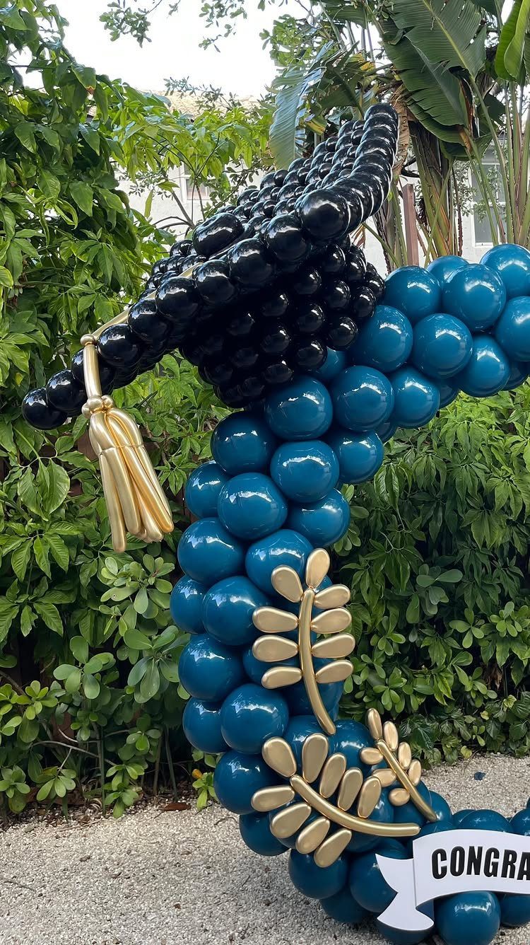 Teal and black balloon sculpture shaped like a graduation cap with gold accents.