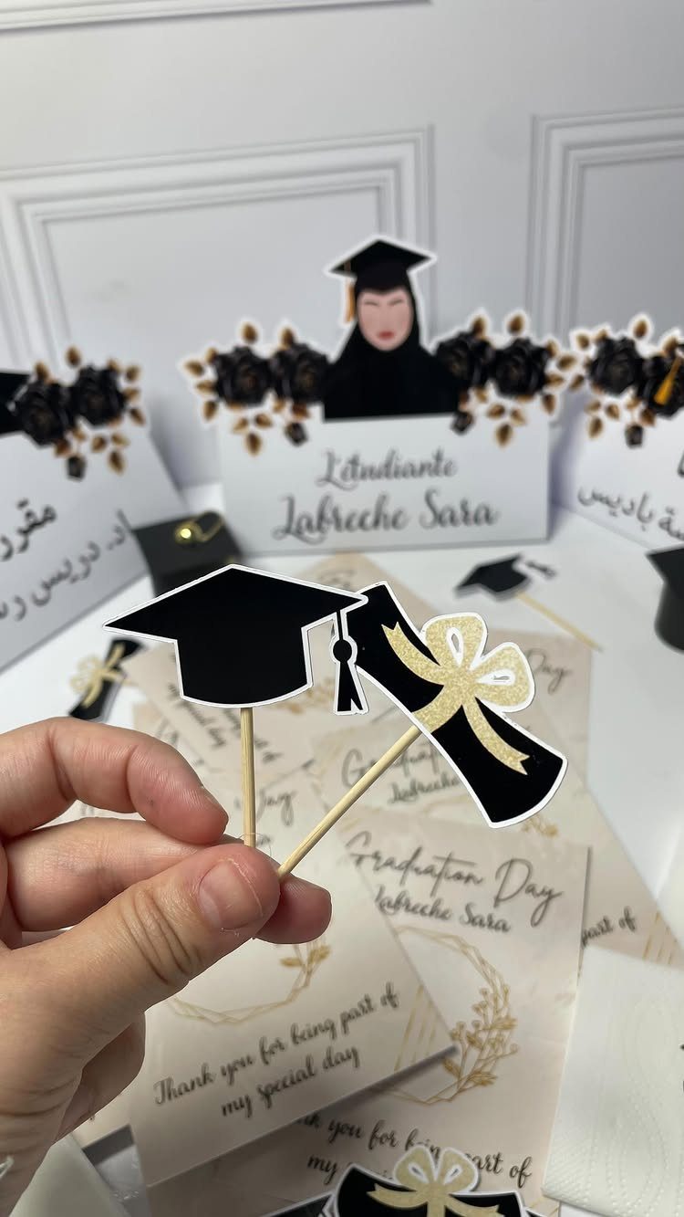 Graduation cap and diploma cupcake toppers held by a hand over party stationery.