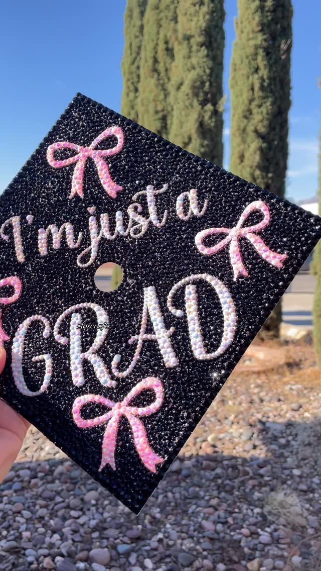 Decorated black graduation cap with pink rhinestone bows and glittery text.