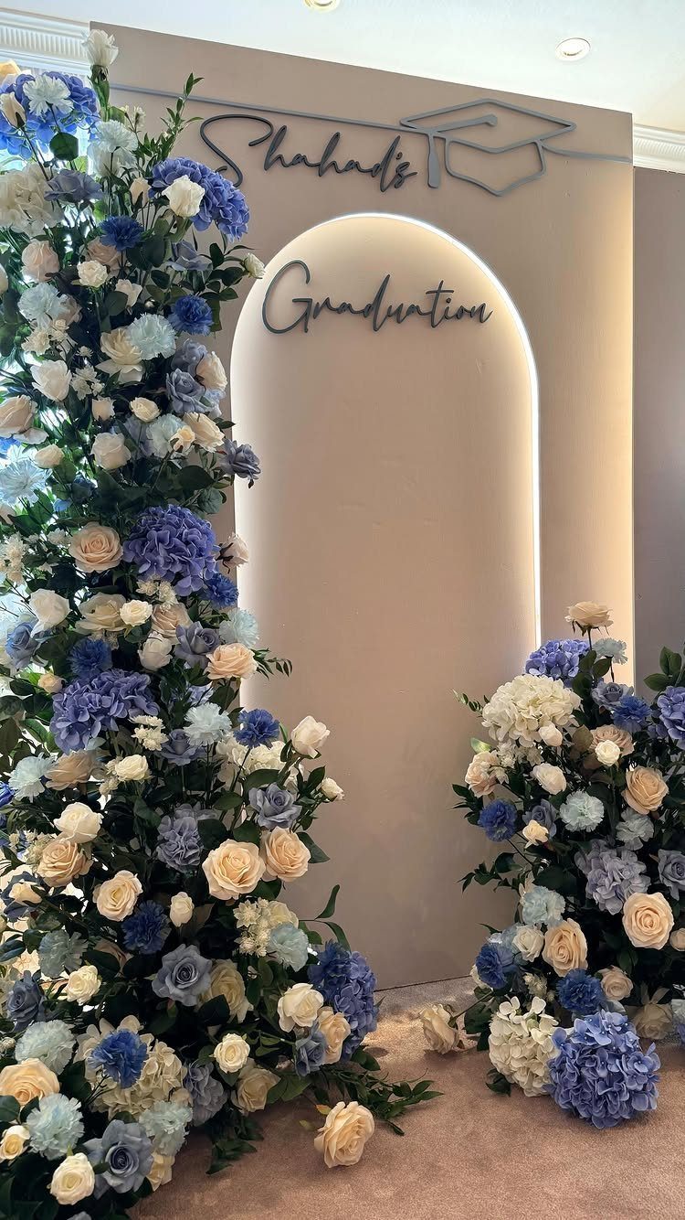 Graduation backdrop with beige arched wall and lush blue and white floral arrangements.